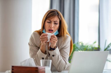 Cropped shot of an attractive young businesswoman sitting alone in her office and coughing as she suffers from a cold. Medical mask and hand disinfectant and stressed woman. Businesswoman working in her office while suffering from allergies clipart