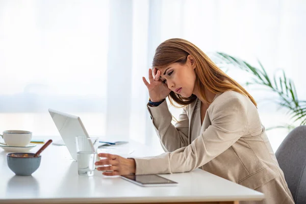 Tired businesswoman rubbing eyes in office. Shot of a young businesswoman looking overly stressed in her office. Stressed female corporate employee having migraine