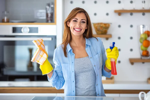 Young woman doing house chores. Woman holding cleaning tools. Woman wearing rubber protective yellow gloves, holding rag and spray bottle detergent. It\'s never too late to spring clean