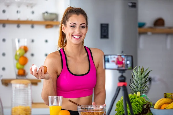 Bir fitness kadını tavuk yumurtalarını gösteriyor. Onları elinde tutuyor ve arka planda da bir mutfak var. Gülümseyen Kadın Yumurta Tutuyor. Fitness kadını sağlıklı bir kahvaltı hazırla..