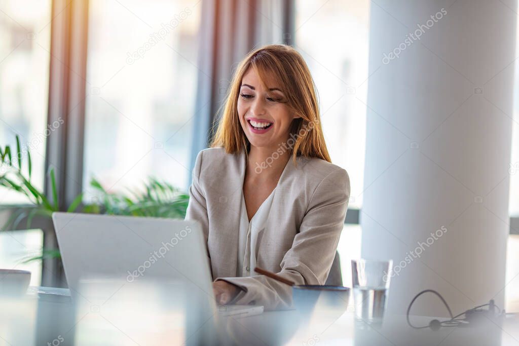Portrait of a happy businesswoman working at her office desk. Beautiful smiling mixed race businesswoman dressed casual sitting in office and using laptop.