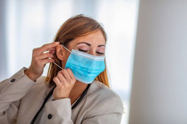 Gribi önlemek için mavi bir tıbbi maske takan beyaz kadının detaylı fotoğrafı. Bulanık arka plan, maskeye odaklan. Coronavirus, COVID-19 karantinası. Doktor, hemşire konsepti.