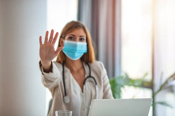 Doctor wears mask with stop symbol. A female doctor with a surgical mask is making a stop sign. Quarantine due to Corona virus. Doctor\'s hand selective focus area. Doctor holding mask with stop symbol