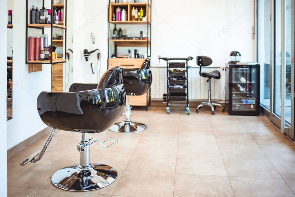 Empty black chairs and mirrors in barber shop. Interior of illuminated hair salon. Interior of modern hair salon. Empty interior of modern hairdressing salon