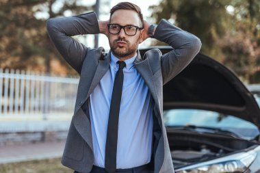 Takım elbiseli profesyonel bir erkek beklenmedik bir araba sorununa tepki verir ve dışarıda endişeli görünür. Yakalama profesyonelliği, beklenmedik durumları ve işin dengelenmesinin zorluklarını beklenmedik koşullarla taşır..