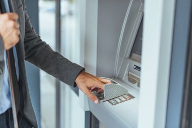 Profesyonel giyimli bir birey, finansal amaçlar, kolaylık, teknoloji ve modern bankacılık için otomatik veznedar (ATM) işletir..