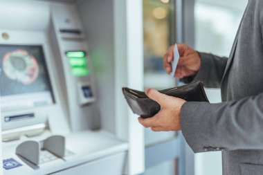 Resmi kıyafetleri olan bir adam ATM 'den para çekmiş, elinde kredi kartı ve cüzdan varmış. Günlük yaşamda bankacılık, finans ve güvenli işlemleri temsil eder.