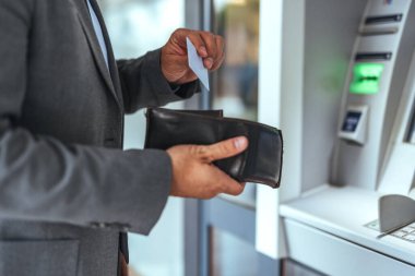 Bir ATM makinesinde iyi giyimli bir profesyonel, bir cüzdan tutuyor ve bir makbuzu inceliyor, finansal faaliyetleri, banka işlemlerini ve modern hayattaki kişisel işlemlerini sembolize ediyor..