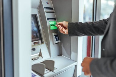 Bankamatik işleten bir adam, bir kart ekleyerek, teknoloji, finans ve bankacılık hizmetlerini temsil ederek, kolaylık ve modern iş uygulamalarına odaklanarak,.