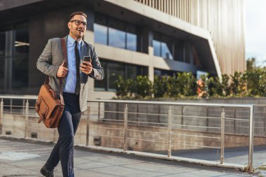 Kendine güvenen bir iş adamı modern bir ofis binasının önünde akıllı bir telefon tutuyor. Profesyonel kıyafette iletişim, verimlilik ve şehir yaşam tarzını gösterir.