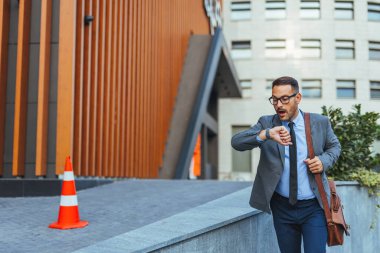 İş dünyasından profesyonel bir adam modern bir şehir ortamında yürürken saatine bakar, aciliyet ve dinamik bir yaşam tarzını önerir..