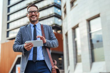 Açık havada tablet kullanan, modern iş teknolojisi ve kentsel yaşam tarzını sergileyen resmi giyinmiş kendine güvenen bir iş adamı..