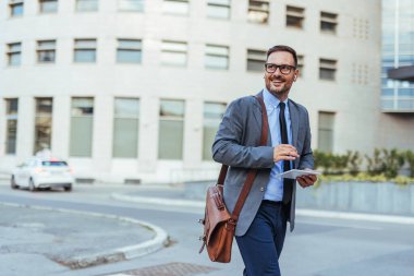 Profesyonel bir işadamı, elinde bir tablet, gülümseyerek, başarıyı ve modern şehir yaşam tarzını somutlaştırarak şehirde rahatça dolaşır..