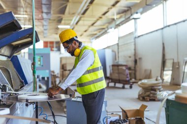 Parlak bir endüstriyel ortamda üretim makinelerini denetleyen mühendis, üretim süreçlerinde güvenlik, verimlilik ve ileri teknolojiyi vurguluyor..