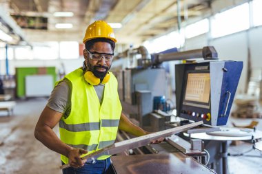 Fabrika işçisi, fabrika ortamında güvenlik teçhizatı kullanırken makine kullanıyor, profesyonelliği, teknolojiyi ve işyeri güvenliğini gösteriyor.