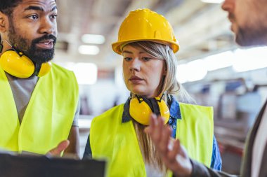 Bir fabrikada güvenlik ekipmanı kullanan bir grup işçi, güvenlik ve verimliliği artırma, takım çalışması ve endüstriyel düzenlemelere uyma amaçlı işyeri süreçleri hakkında bir tartışmaya girişiyor..