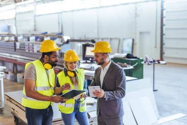 İnşaat ekibi modern bir endüstriyel tesiste proje detaylarını tartışıyor, takım çalışmasını ve güvenlik bilincini destekliyor.