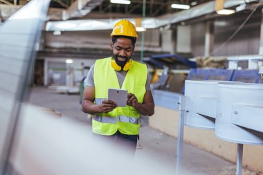 Fabrika ortamında tablet kullanan profesyonel bir iş adamı, imalat ve işçi güvenliği teknolojisini vurguluyor..