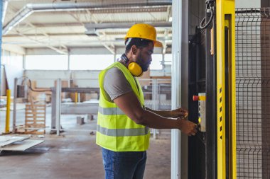 Güvenlik donanımı giyen bir işçi, güvenlik ve hassasiyeti vurgulayarak, temiz ve geniş bir endüstriyel tesiste makineler çalıştırıyor..