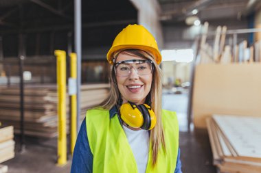 İnşaat alanında çalışan, güvenlik kaskı, gözlük ve kulaklık takan, profesyonelliği, güvenlik dayanışmasını ve endüstriyel iş gücünü temsil eden parlak bir iş yerinde gülümseyen kendine güvenen kadın işçiler..