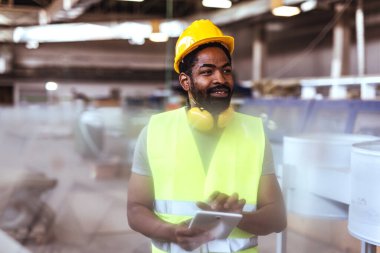 Modern bir imalat ortamında tablet kullanırken çelik yelek, çelik yelek ve eldiven giyen kendinden emin bir sanayi işçisi. Endüstriyel ortamlarda teknoloji entegrasyonunun mükemmel tasviri.