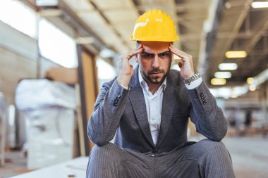 Resmi takım elbiseli ve şapkalı profesyonel bir adam, bir inşaat sahasında düşünceli bir pozda oturuyor, stresi, mühendislik sorunlarını ya da işyerindeki odaklanma sorunlarını vurguluyor.