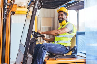 Bir depoda çalışan kendinden emin bir forklift operatörü, ağır makineler kullanırken güvenlik farkındalığı sergiliyor. Koruyucu güvenlik giysileri içinde, pozitif ve profesyonel bir tavır sergiliyor..