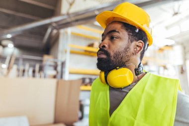 Güvenlik yeleği ve sert şapkalı erkek inşaat işçisi, endüstriyel bir depo ortamında işyeri güvenliğinin sağlanması.