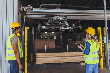 Güvenlik teçhizatı takan iki sanayi işçisi bir depodaki otomatik makine sistemini denetliyor. Kurulum sanayi operasyonları, işyeri güvenlik protokolleri ve gelişmiş üretim teknolojisinin uygulanmasını vurguluyor.