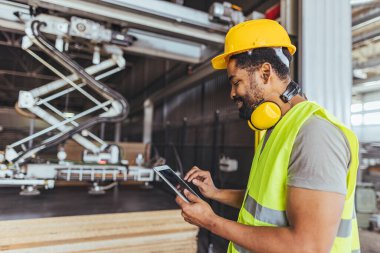 Yüksek görüş açısına sahip yelek ve sanayi makinelerini tablet kullanarak çalıştıran bir mühendis..