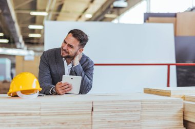 Profesyonel mimar malzemeleri kontrol ederken tabletle çalışıyor. Parlak ve modern atölye ortamı, tasarım, yaratıcılık ve verimliliği tasvir ediyor. Masadaki başlık güvenlik ve inşaatı simgeliyor..