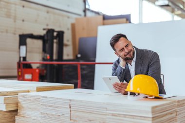 Profesyonel bir mühendis ya da yönetici endüstriyel çalışma alanındaki bir tabletin planlarını gözden geçirir. İnşaat ve üretkenliği vurgulayan imaj, liderlik, planlama ve çalışkan takım çalışmalarının yorumlarını davet ediyor..