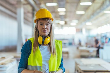 İnşaat alanında çalışan, güvenlik kaskı, gözlük ve kulaklık takan, profesyonelliği, güvenlik dayanışmasını ve endüstriyel iş gücünü temsil eden parlak bir iş yerinde gülümseyen kendine güvenen kadın işçiler..