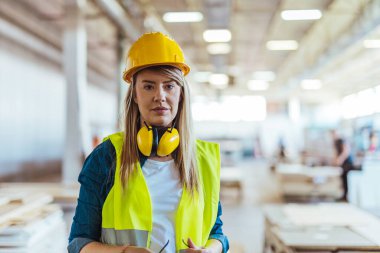 İnşaat alanında çalışan, güvenlik kaskı, gözlük ve kulaklık takan, profesyonelliği, güvenlik dayanışmasını ve endüstriyel iş gücünü temsil eden parlak bir iş yerinde gülümseyen kendine güvenen kadın işçiler..