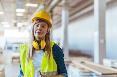 İnşaat alanında çalışan, güvenlik kaskı, gözlük ve kulaklık takan, profesyonelliği, güvenlik dayanışmasını ve endüstriyel iş gücünü temsil eden parlak bir iş yerinde gülümseyen kendine güvenen kadın işçiler..