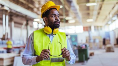 İnşaat alanında güvenlik kaskı ve gözlüklü Afro-Amerikan mimar.