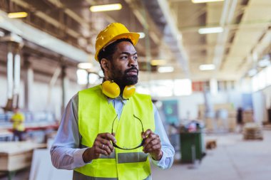 İnşaat alanında güvenlik kaskı ve gözlüklü Afro-Amerikan mimar.