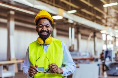Fabrikada koruyucu miğferli gülümseyen genç erkek mühendisin portresi..