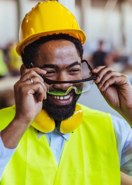 İnşaat alanında güvenlik kaskı ve gözlüklü Afro-Amerikan mimar.