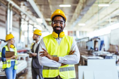 Gülümseyen Afro-Amerikan erkek işçi, profesyonel giyimli ve güvenlik teçhizatlı.