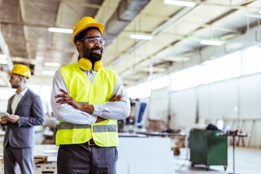 Gülümseyen Afro-Amerikan erkek işçi, profesyonel giyimli ve güvenlik teçhizatlı.