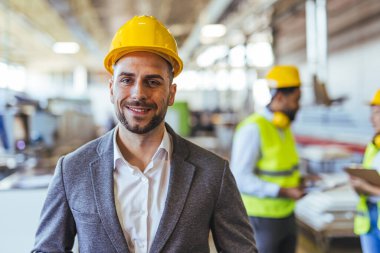 Kask takan bir mühendis endüstriyel bir ortamda güvenle duruyor ve işleri denetliyor. Sanayi ortamında işbirliği yapan, takım çalışmasını ve profesyonelliği vurgulayan bir ekip yer alıyor.