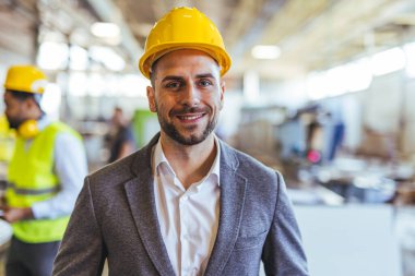 İnşaat alanında profesyonel bir mühendis, sıkı bir şapka ve takım elbise giyiyor, kendine güven ve liderlik gösteriyor. Çalışma ortamı endüstriyel ve profesyonel çevreyi vurguluyor.