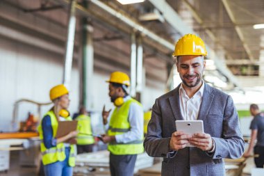 Bir şantiyede proje detaylarını gözden geçiren, endüstriyel bir ortamda liderlik ve takım çalışması sergileyen, güvenlik donanımlı bir grup inşaat çalışanı..