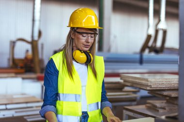 Fabrikada kasketli, koruyucu gözlüklü ve kulak koruyucu takan bir kadın işçi.. 