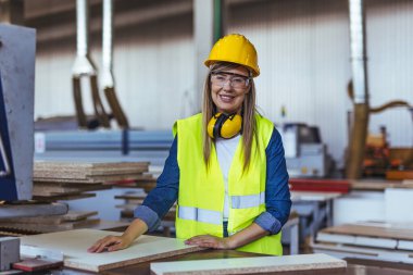 Bir fabrika ortamında, koruyucu gözlük takan ve kulaklık takan bir bayan işçi gülümsüyor. Endüstriyel bir işyerinde güvenlik, pozitiflik ve profesyonellik göstergesi