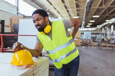 Depoda sarı kasklı ve sırt ağrısı olan Afro-Amerikan erkek mühendis.