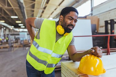 Depoda sarı kasklı ve sırt ağrısı olan Afro-Amerikan erkek mühendis.