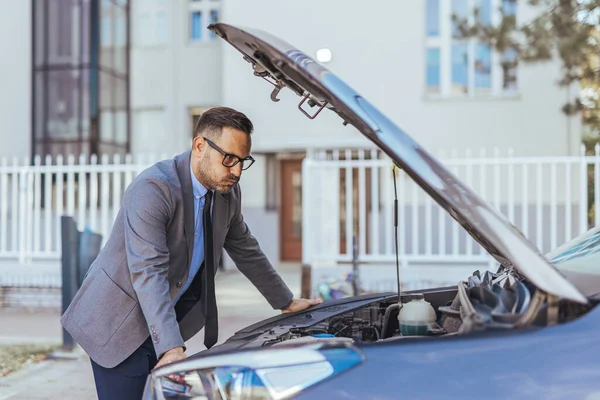 Resmi takım elbiseli profesyonel bir adam, şehir ortamında bir arabanın motor bölmesini inceler ve şirket bağlamında araç işletimi, onarımı veya bakımıyla ilgili sorunlar ortaya çıkarır..
