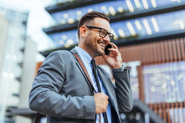 Takım elbiseli profesyonel bir işadamı cep telefonuyla iletişim kuruyor, modern ofis ortamında güven ve karizma yayıyor. Başarı, iletişim ve kurumsal yaşam tarzı temaları için ideal.